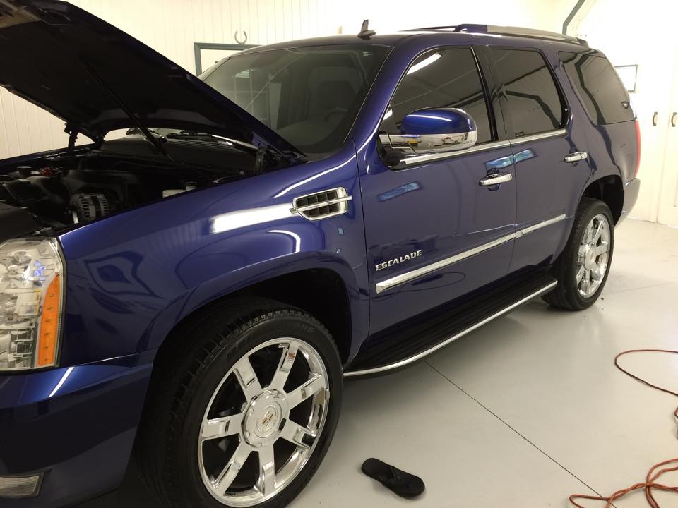 A blue suv with the hood up is parked in a garage.