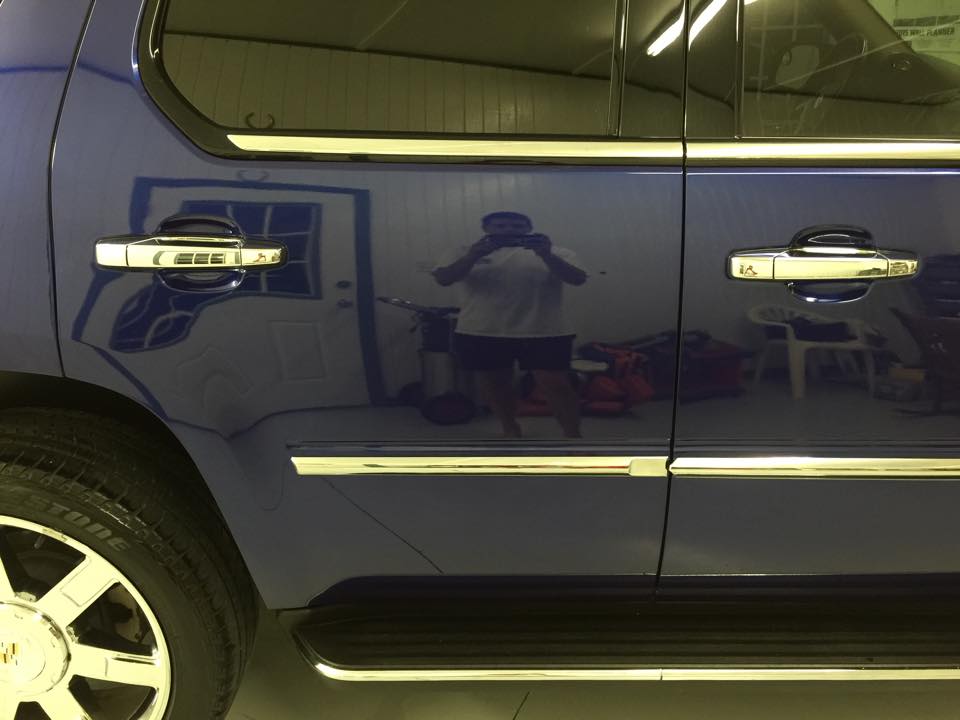 A man is taking a picture of his reflection in the door of a blue suv