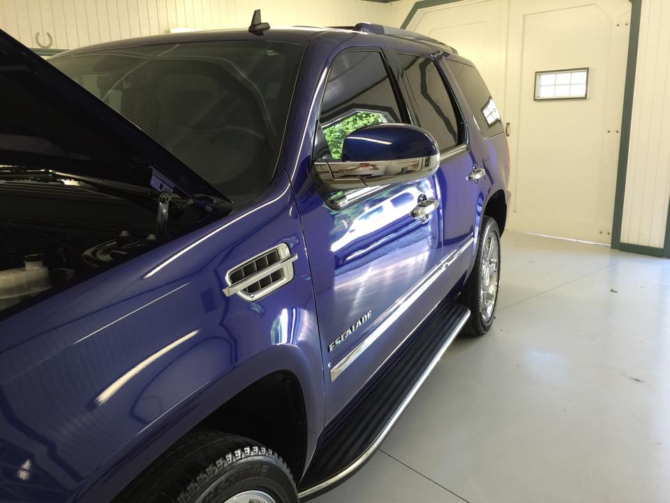 A blue suv with the hood up is parked in a garage