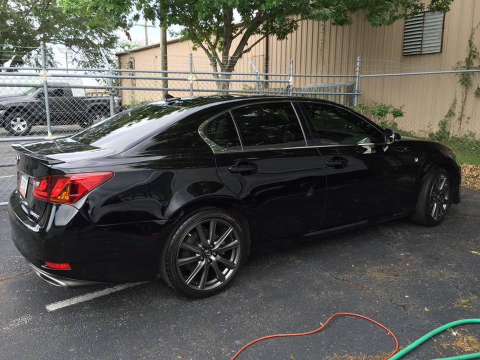 A black car is parked in a parking lot next to a hose.