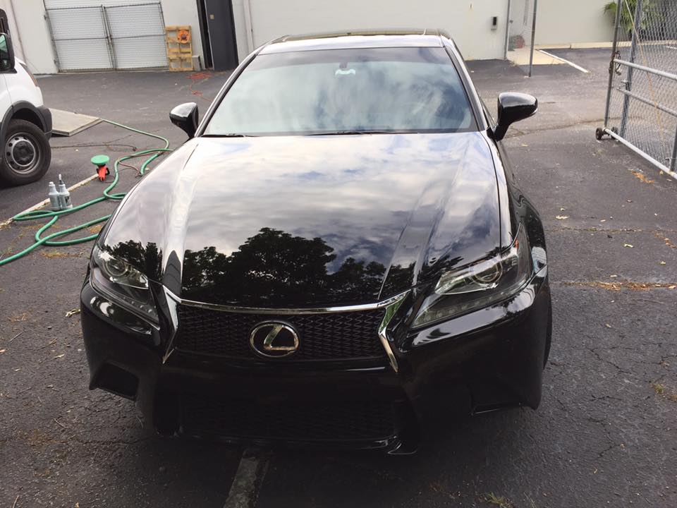 A black lexus is parked in a parking lot next to a hose.