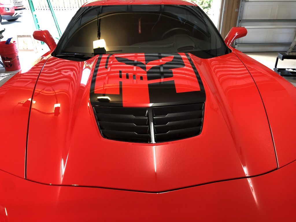 A red sports car with a transformers logo on the hood is parked in a garage.
