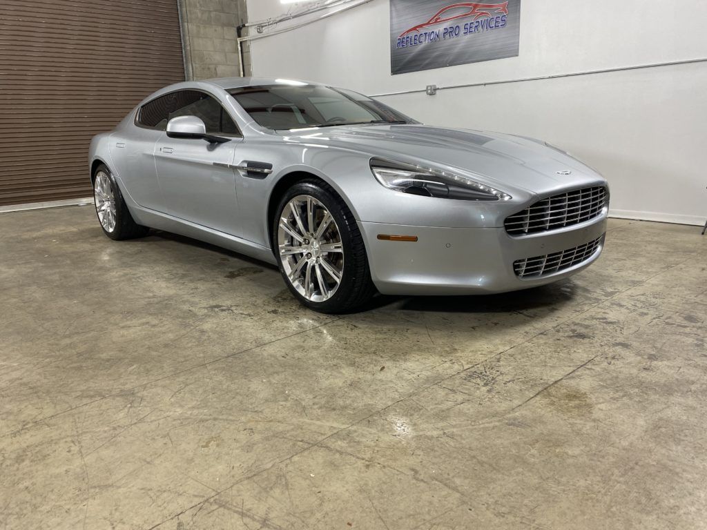A silver aston martin rapide is parked in a garage.