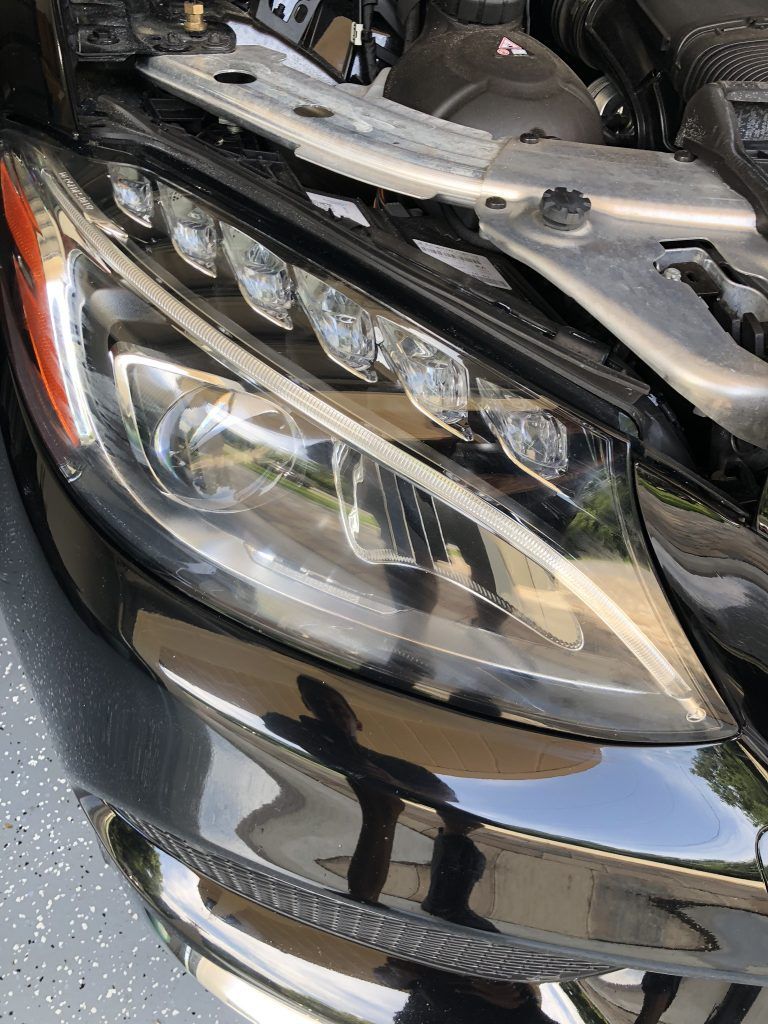 A close up of a car 's headlight with the hood open.