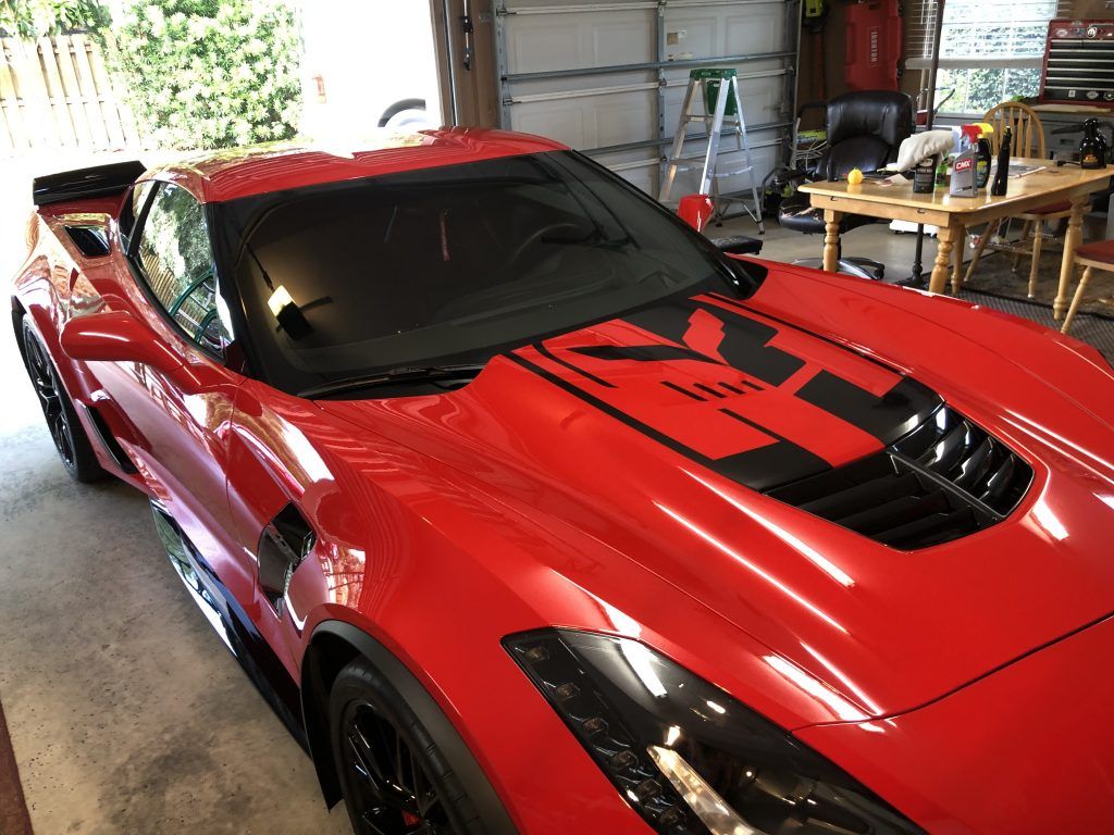 A red sports car with black stripes on the hood is parked in a garage.