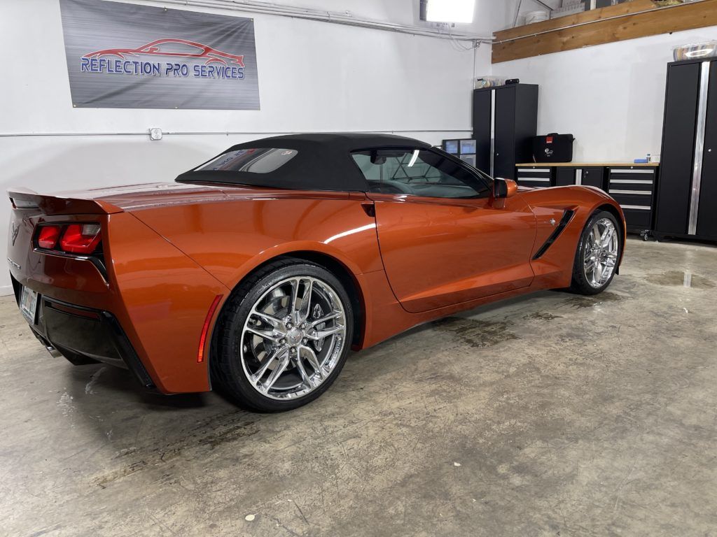 An orange corvette convertible is parked in a garage.