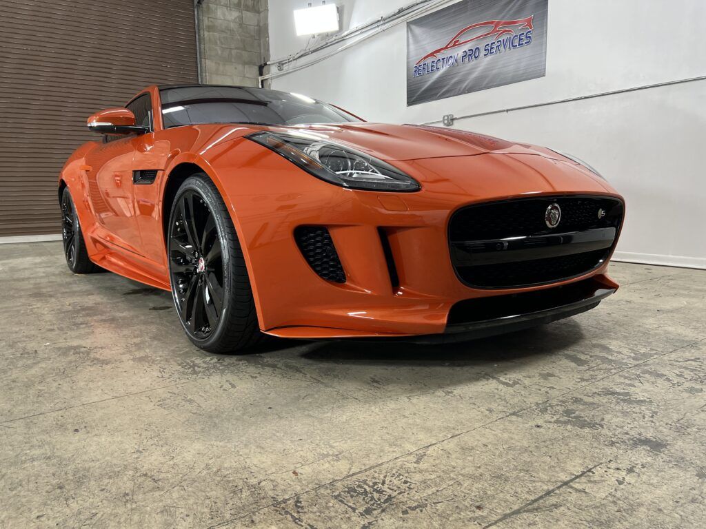 An orange jaguar f type is parked in a garage.