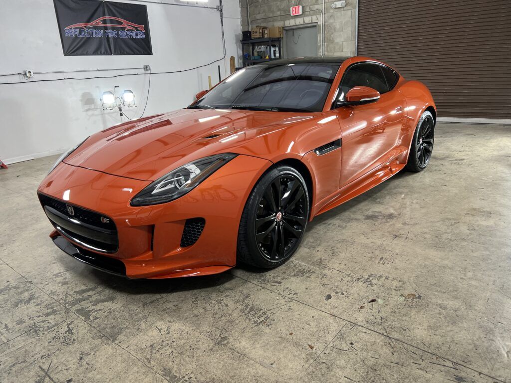 An orange jaguar f type is parked in a garage.