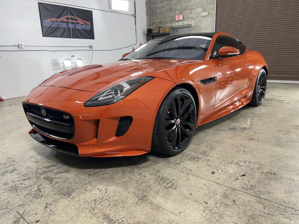 An orange jaguar f type is parked in a garage.