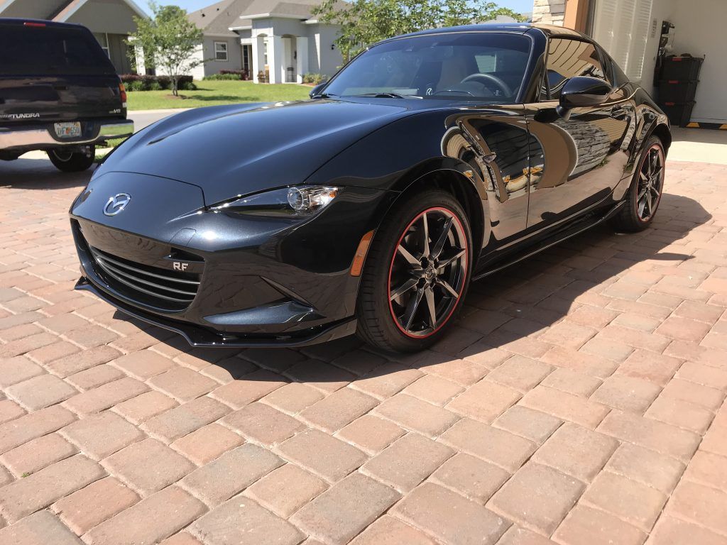 A black sports car is parked on a brick driveway.