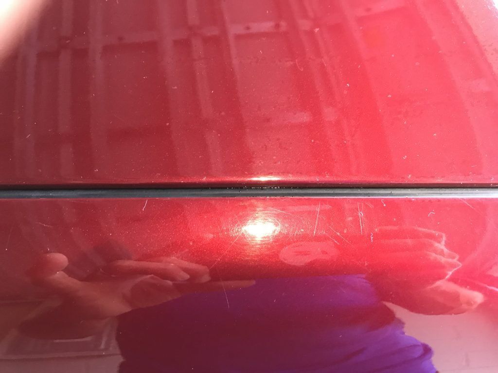 A person is taking a picture of their reflection in a red car.