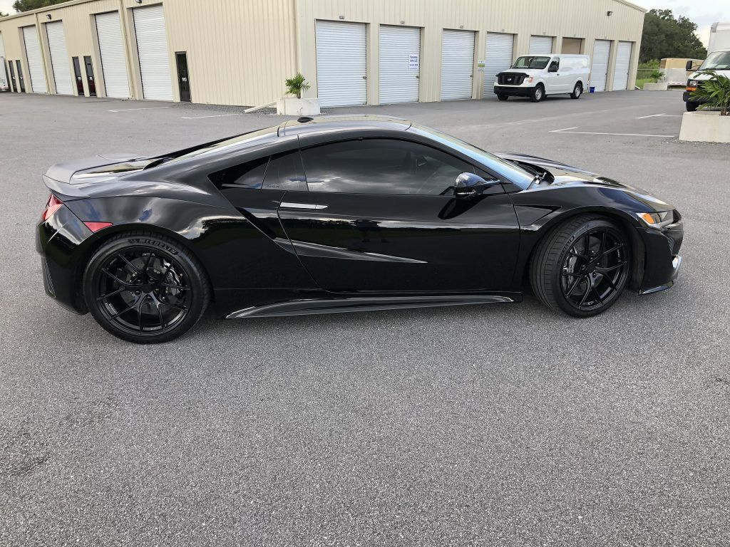 A black sports car is parked in a parking lot in front of a building.