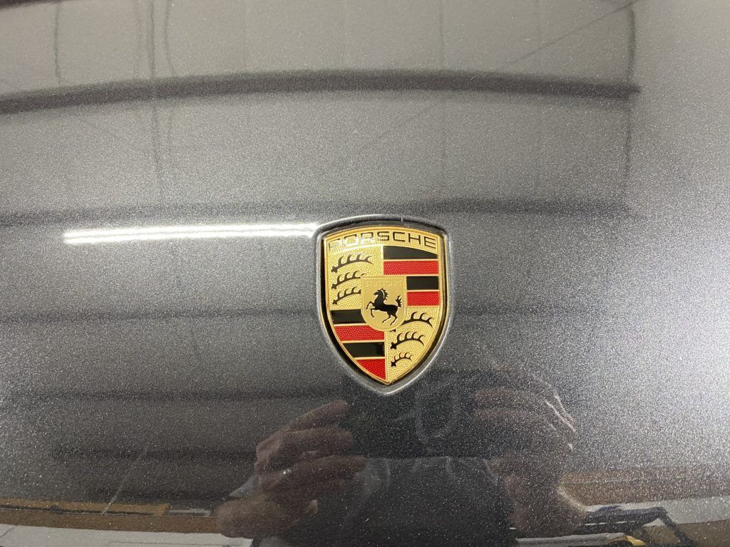 A person is taking a picture of a porsche logo on the back of a car.