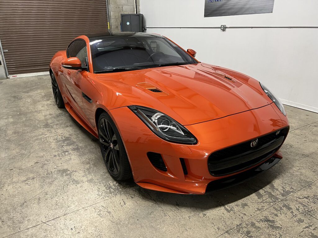 An orange jaguar f type is parked in a garage.