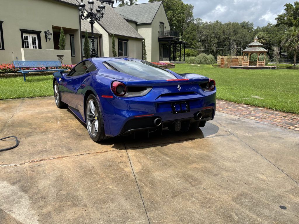 A blue sports car is parked in a driveway in front of a house.