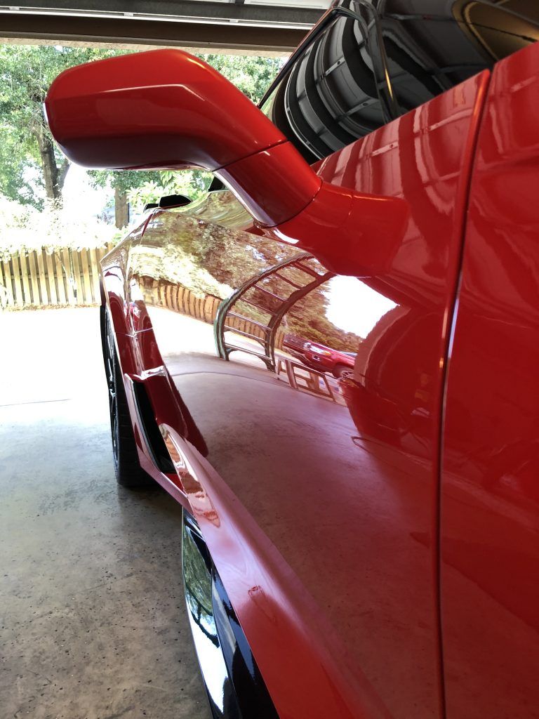 A red car is parked in a garage next to a tire rack