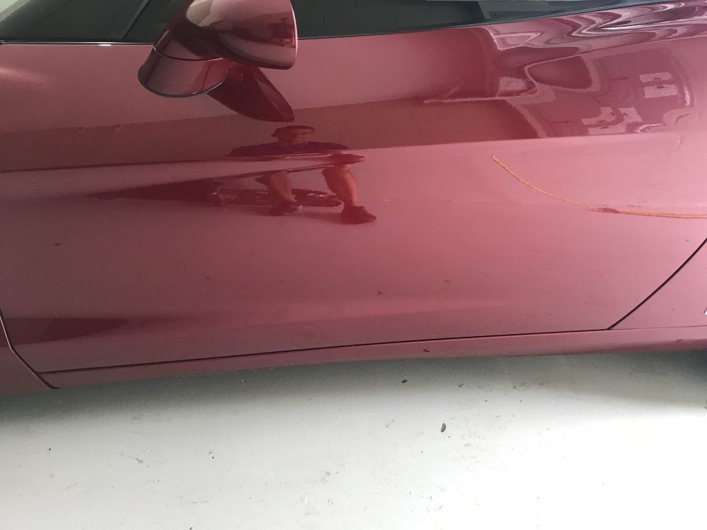 A close up of a red car with a reflection of a person in the door mirror.