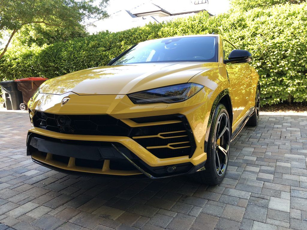 A yellow lamborghini urus is parked on a brick driveway.
