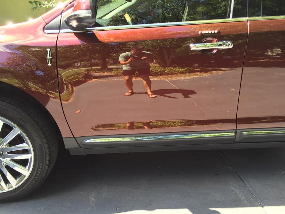 A woman is reflected in the door of a red car