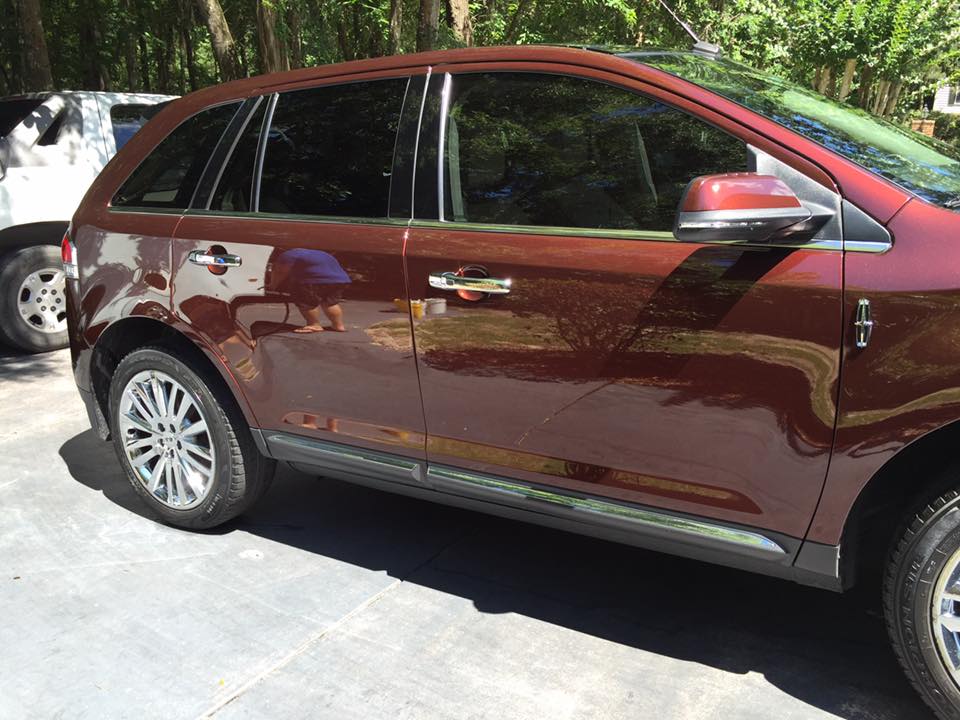 A red car is parked in a parking lot with trees in the background