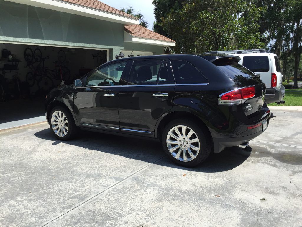 A black car is parked in a driveway in front of a garage.