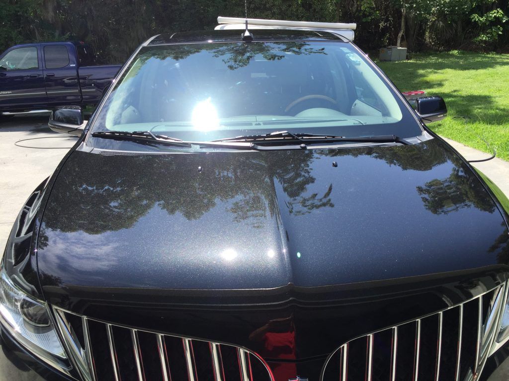 A black car is parked in a driveway with trees in the background