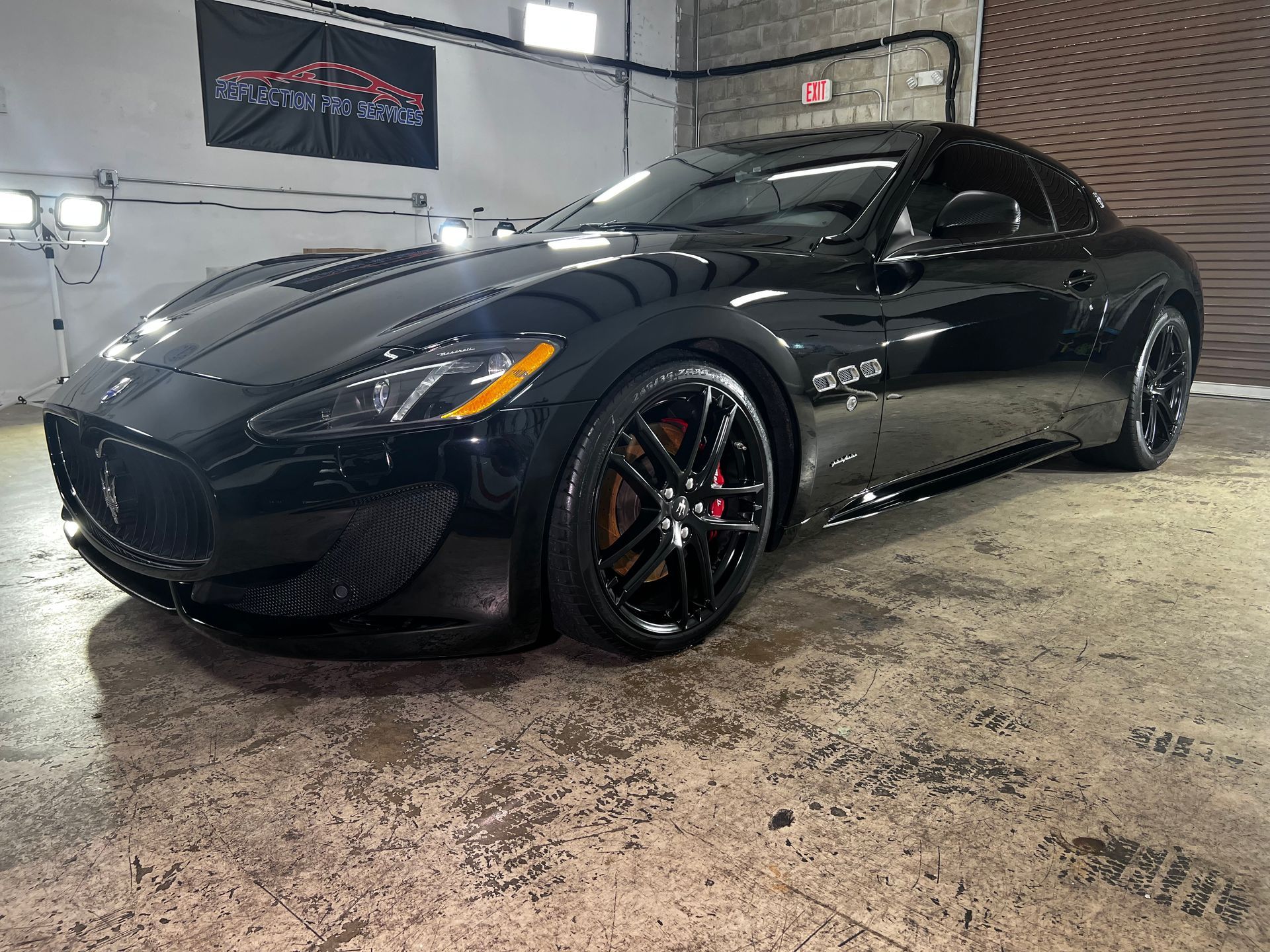 A black maserati granturismo is parked in a garage.