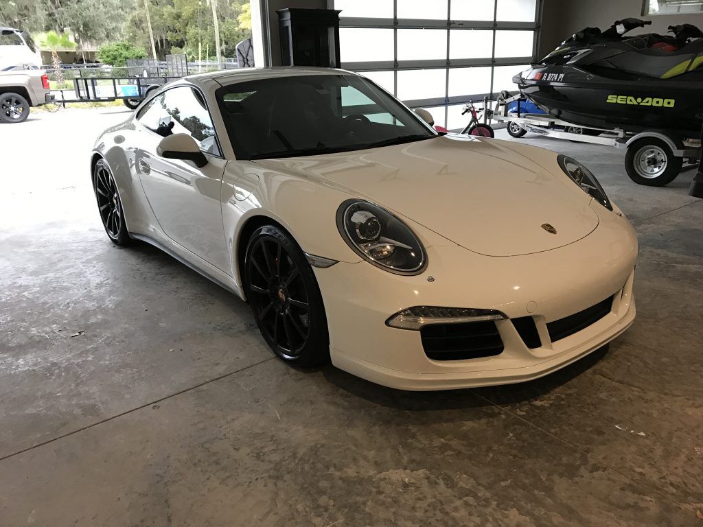 A white porsche 911 gt3 is parked in a garage next to a sea doo jet ski.