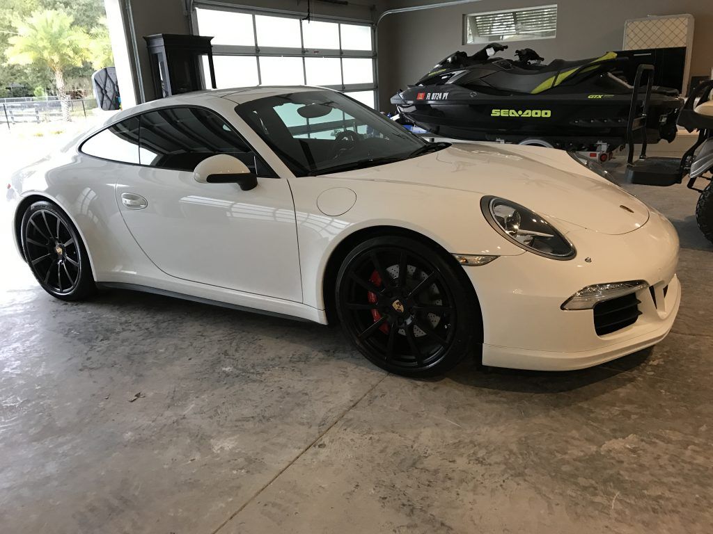A white porsche 911 is parked in a garage next to a jet ski.