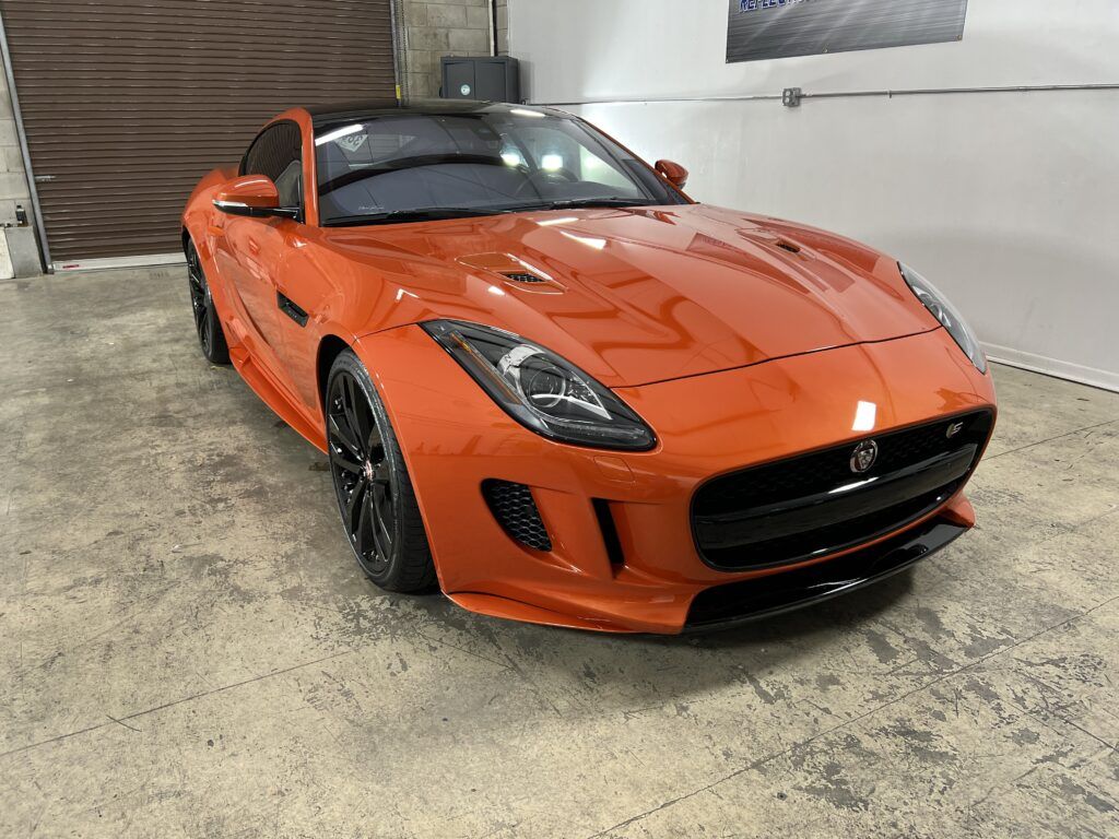 An orange jaguar f type is parked in a garage.