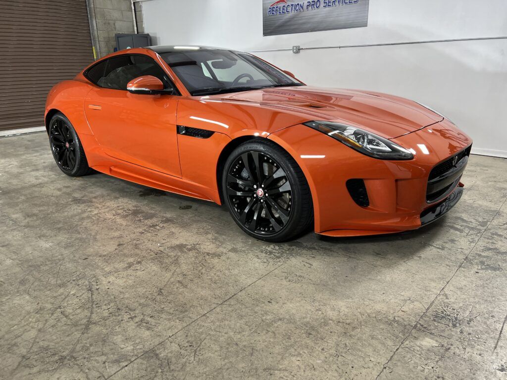 An orange jaguar f type is parked in a garage.