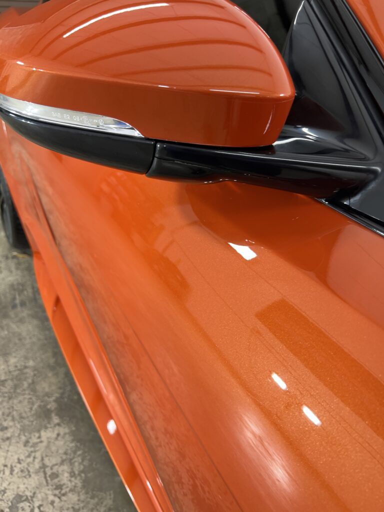 A close up of a side view mirror on an orange car.