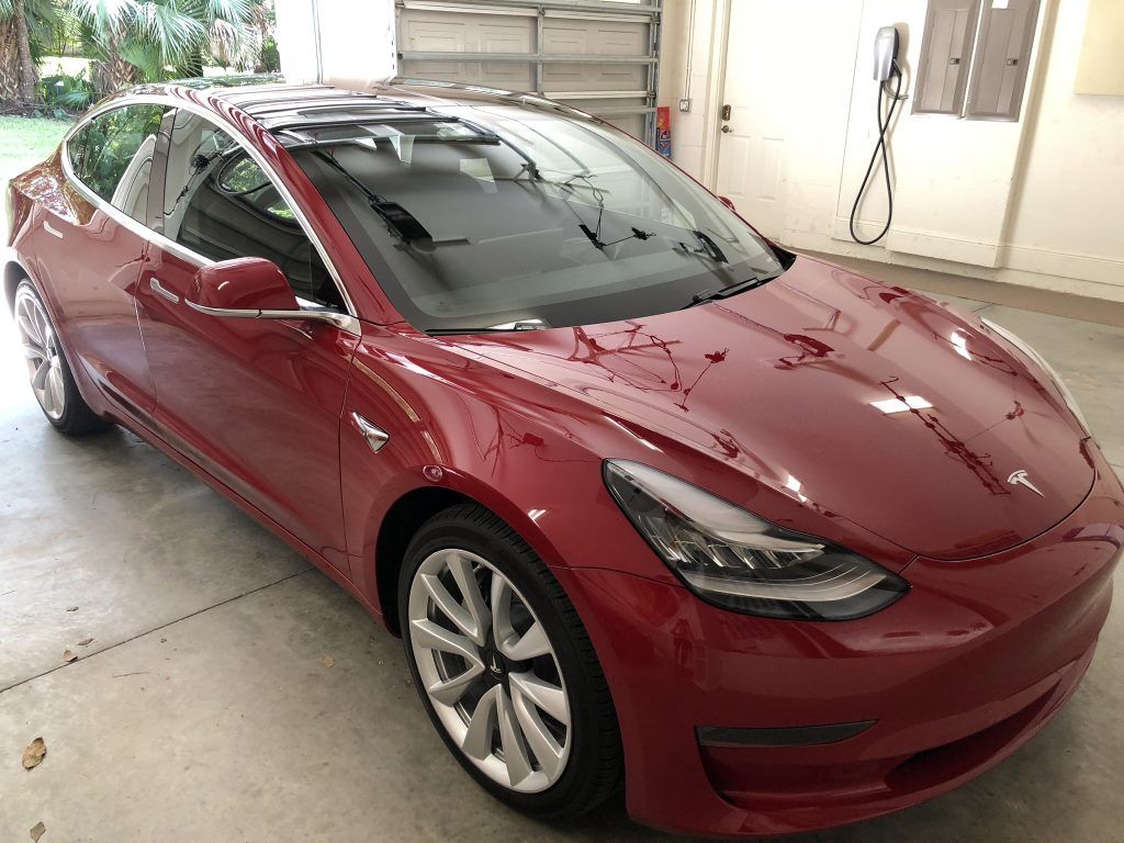 A red tesla model 3 is parked in a garage.