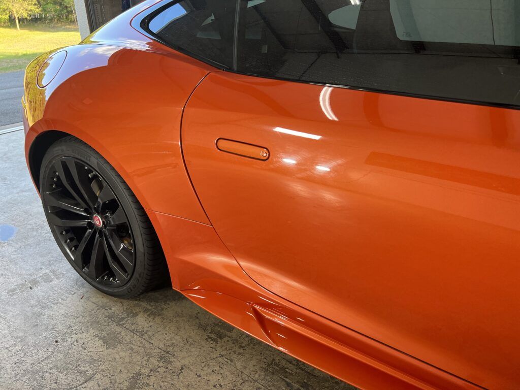 An orange sports car with black wheels is parked in a garage.