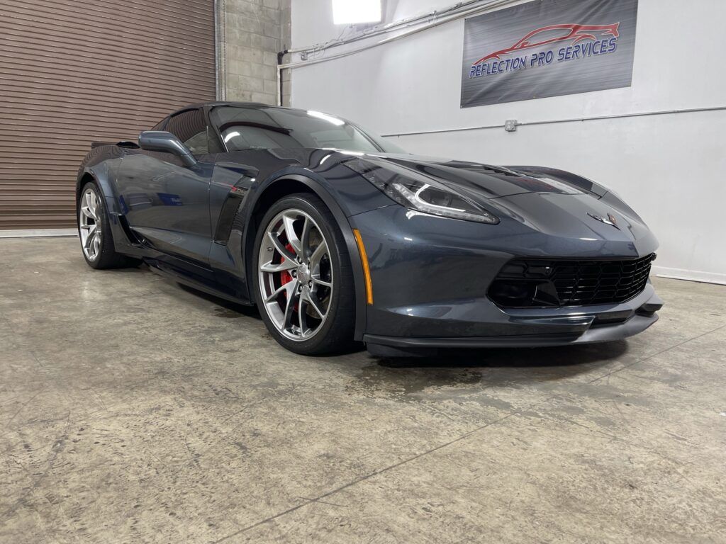 A gray corvette is parked in a garage next to a garage door.