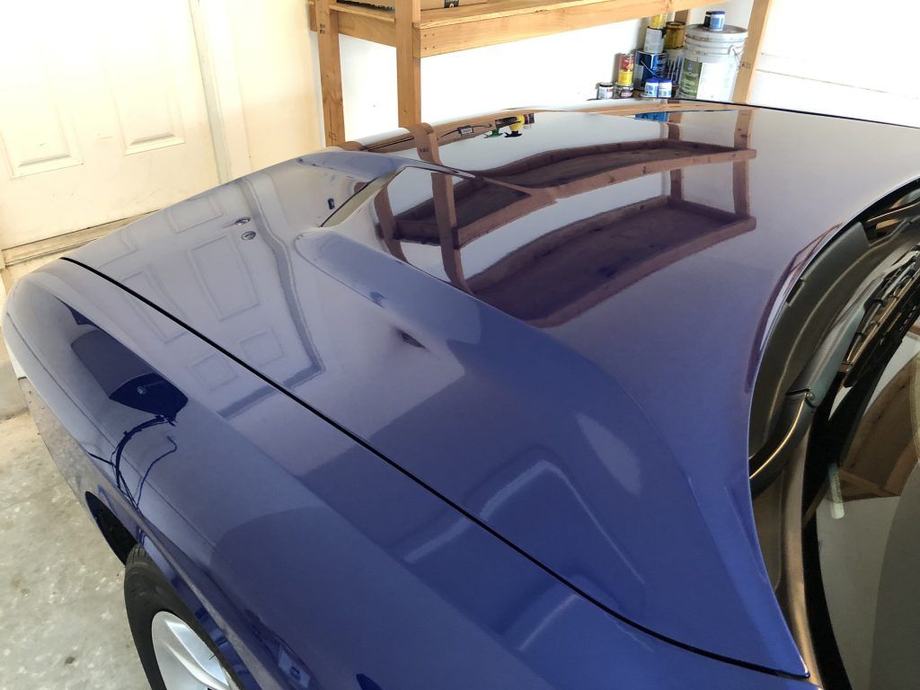 A blue car is parked in a garage with a wooden shelf in the background.