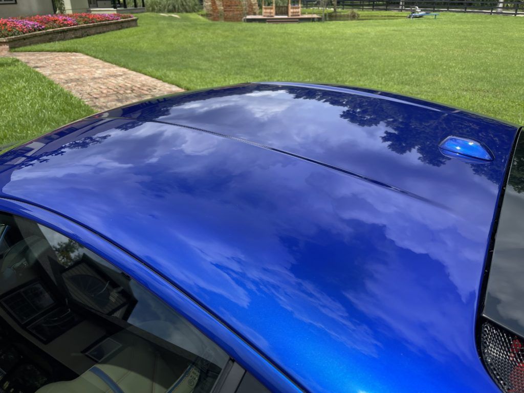 The roof of a blue car is reflecting the sky.
