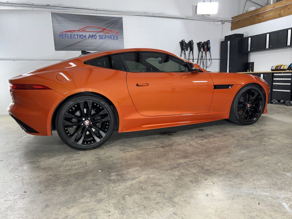 An orange jaguar f type is parked in a garage.