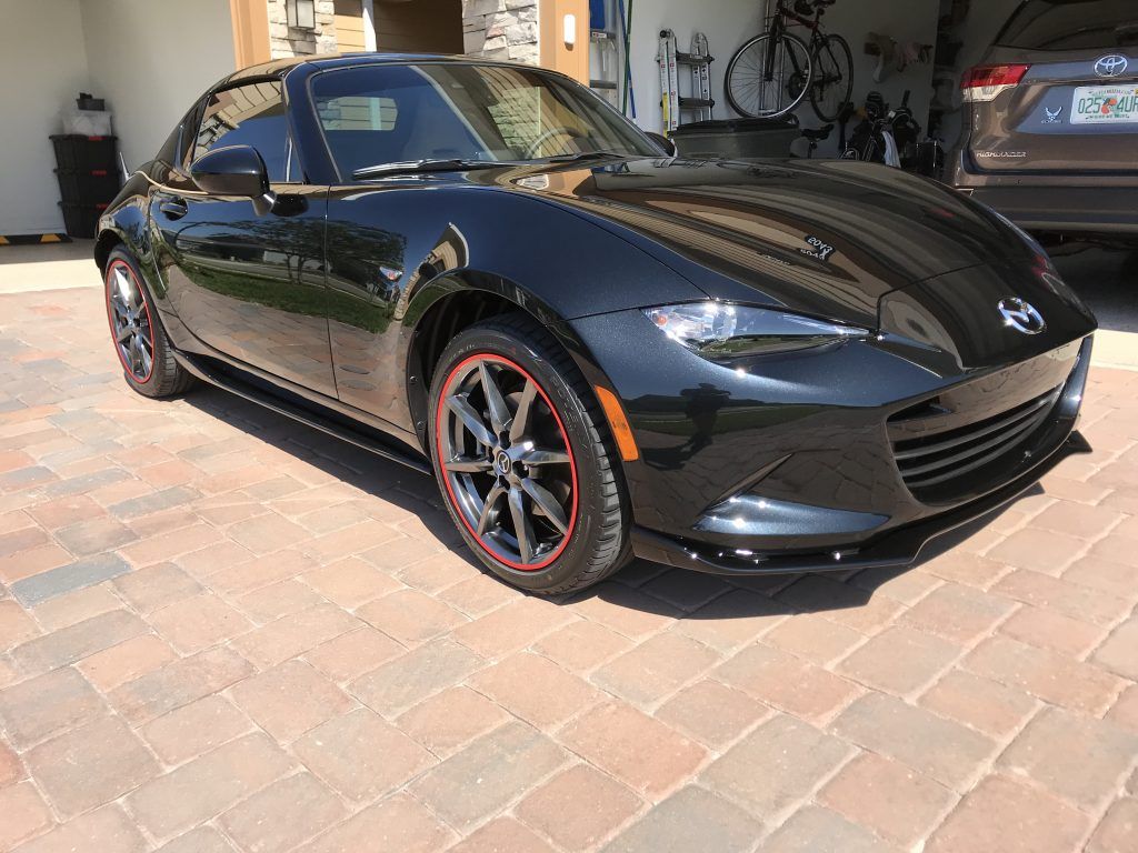 A black sports car is parked on a brick driveway in a garage.