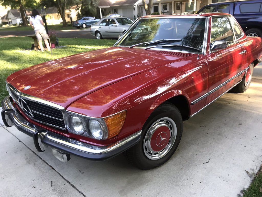 A red car is parked in a driveway in front of a house.