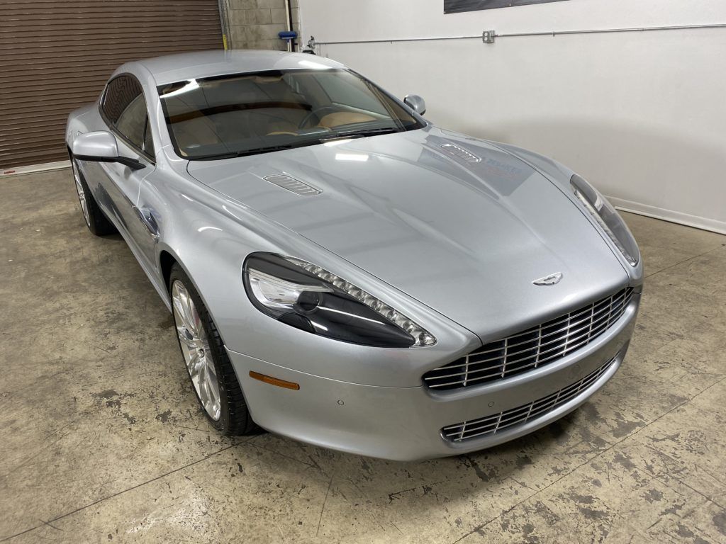 A silver aston martin db9 is parked in a garage.