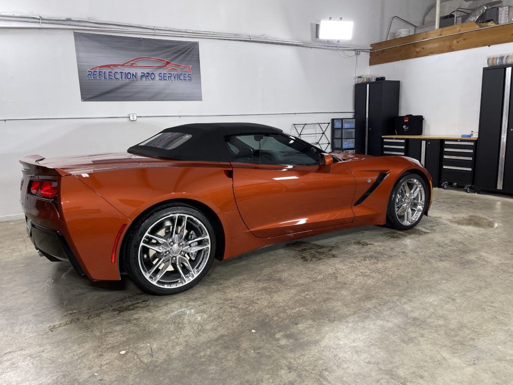 An orange corvette convertible is parked in a garage.