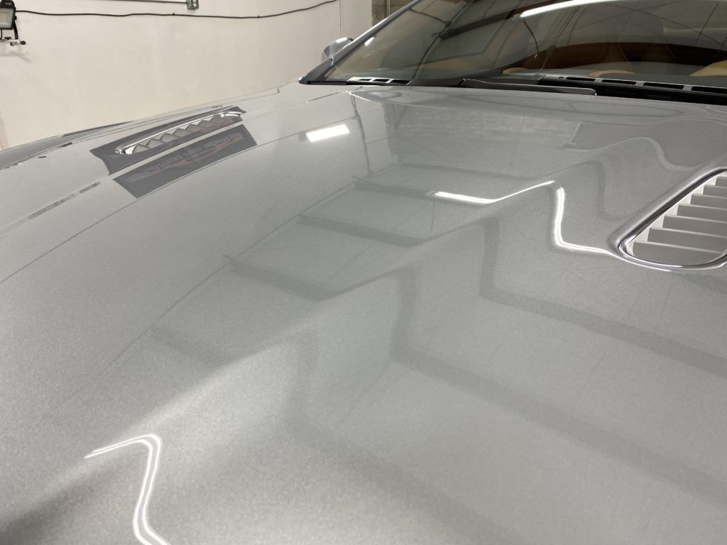 A close up of the hood of a silver car in a garage.