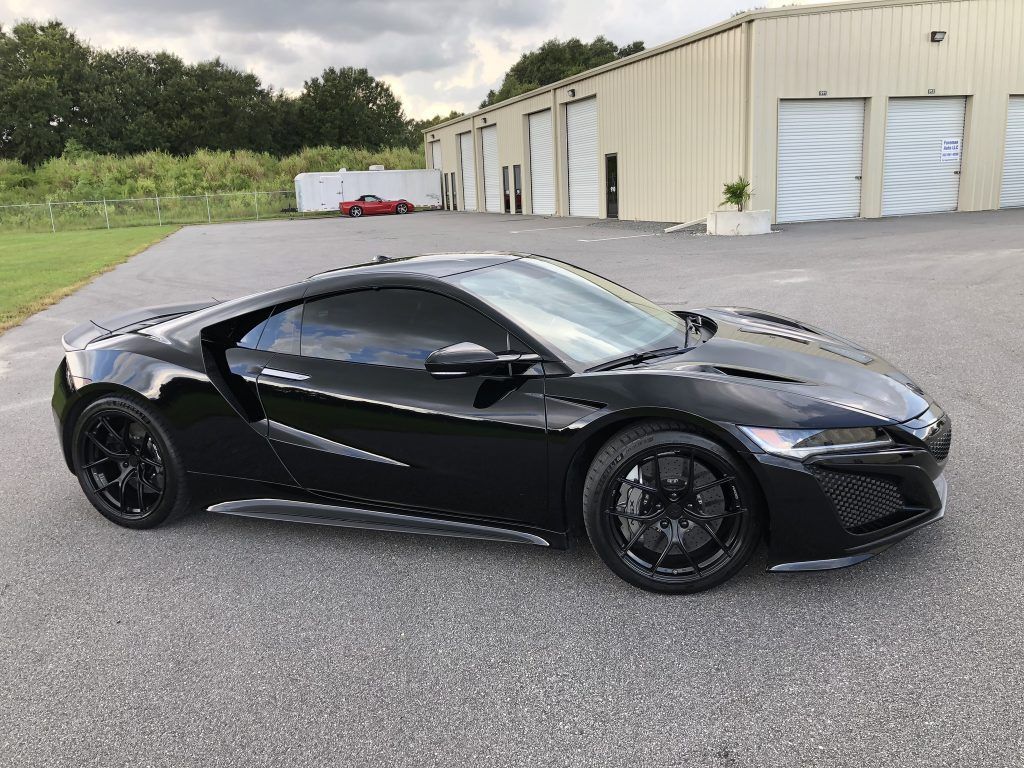 A black sports car is parked in a parking lot in front of a building.
