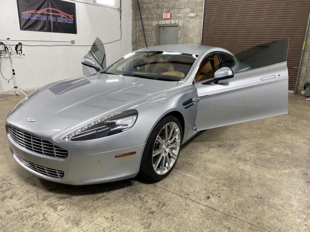 A silver sports car is parked in a garage with its doors open.
