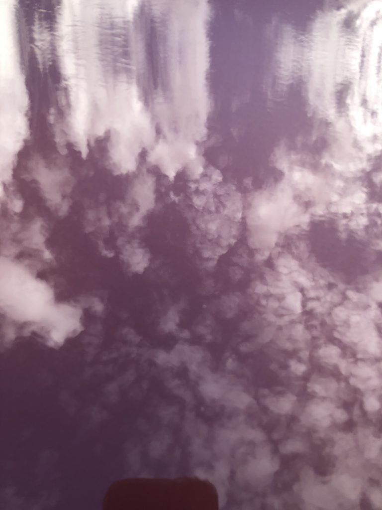 A purple sky with white clouds reflected in the water.