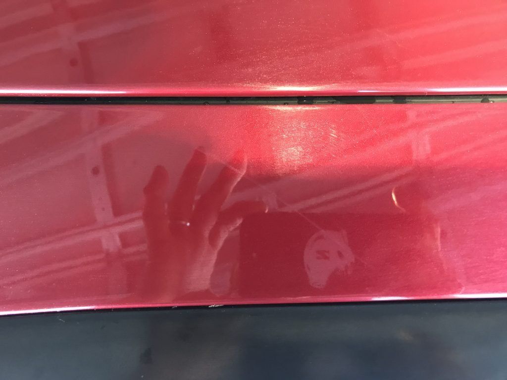 A person is taking a picture of their reflection in a red car door.