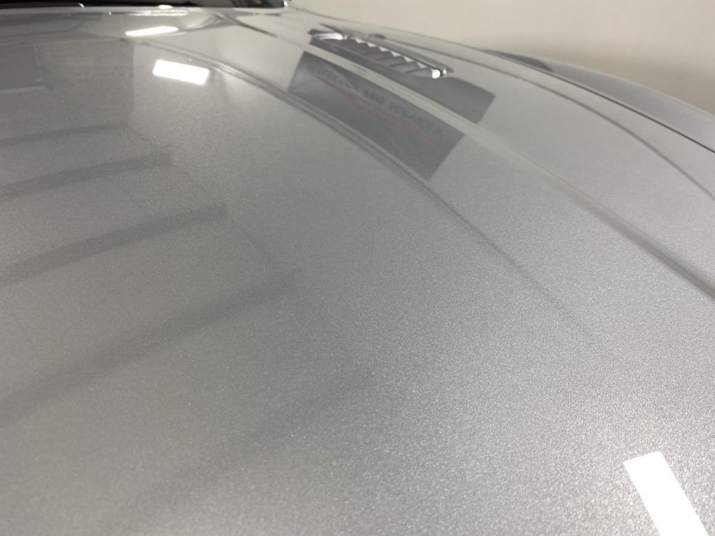 A close up of the hood of a silver car in a garage.