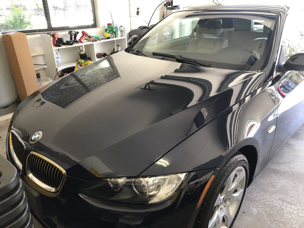 A black bmw is parked in a garage with the hood up.
