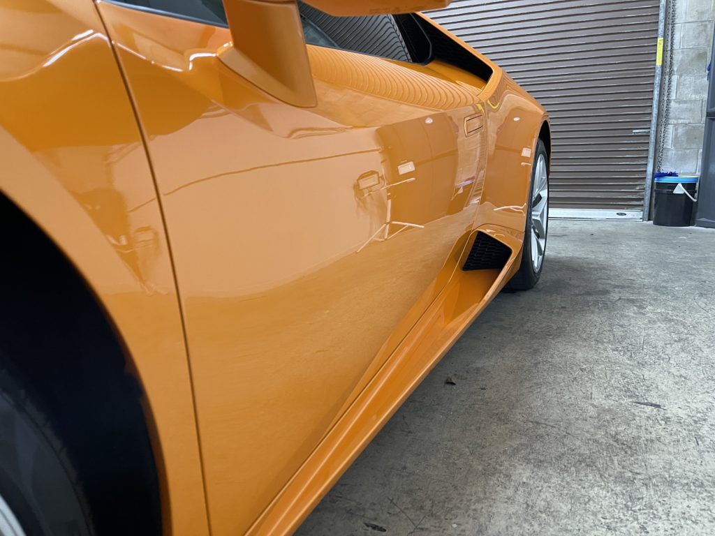 An orange sports car is parked in front of a garage door.
